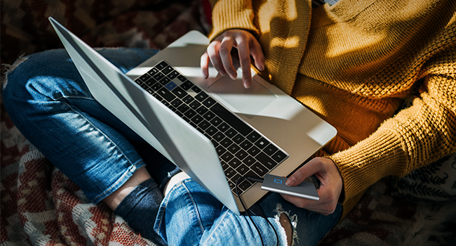 A person with the laptop on their lap and holding the SSD T7 Touch