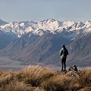 Man standing ontop of mountain looking at snowcapped mountain ranges