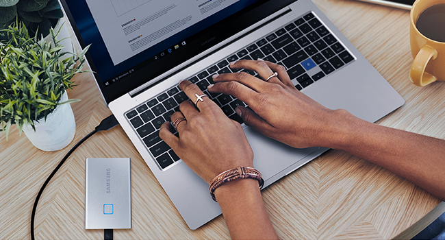 Photo of a laptop, someone's hands on the laptop's keyboard, and a T7 Touch attached to the laptop