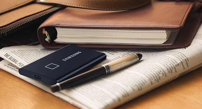 Image of the SSD T7 on a newspaper and a notebook. A pen next to the SSD