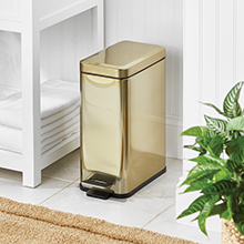 soft brass rectangular step trash can in a bathroom setting, white stand, towels, plant, white walls