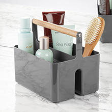 grey shower caddy, wood handle, holding brush, bath bottles, tubes on gray counter, mirror in back